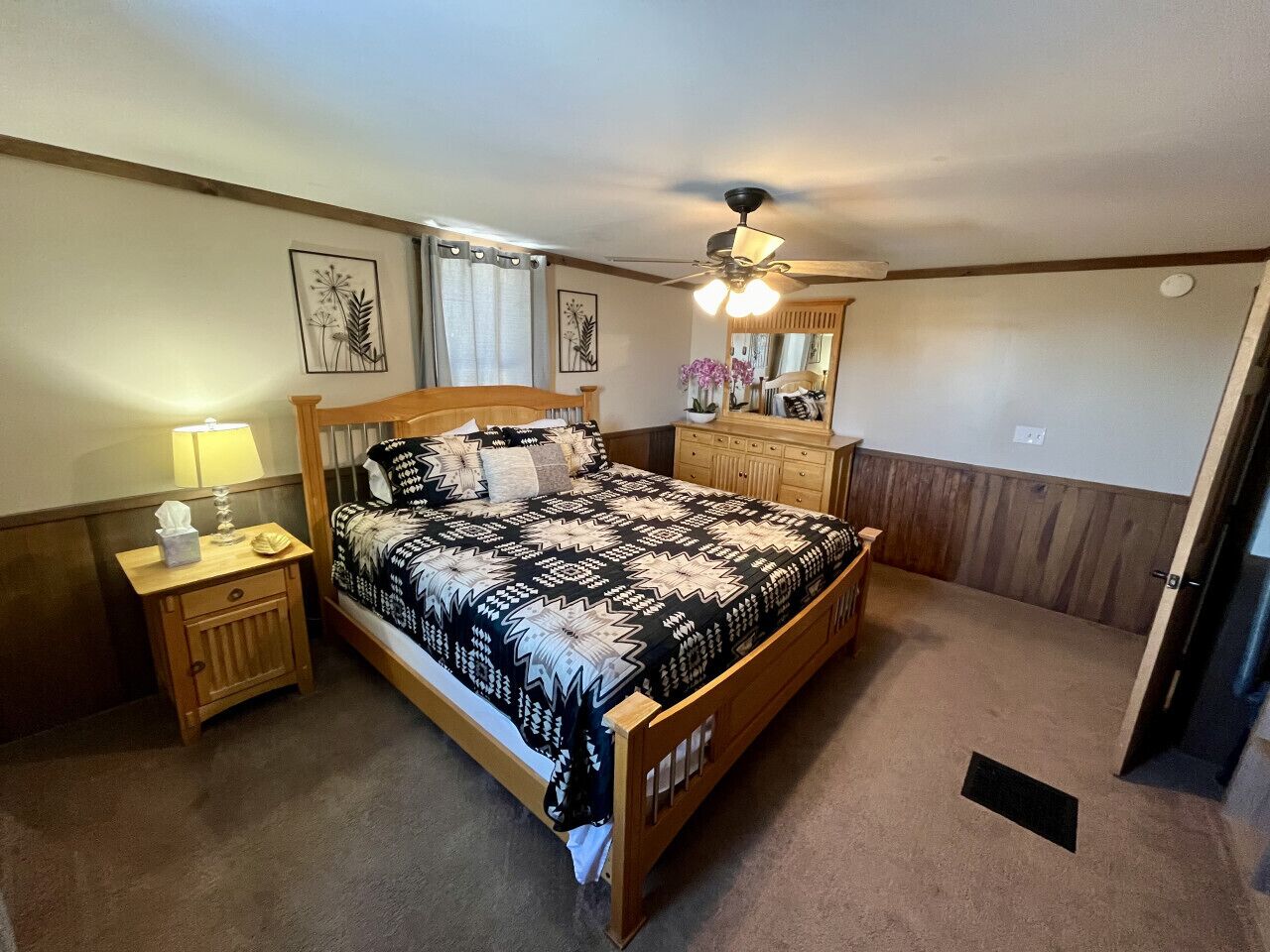 Ein Schlafzimmer mit einem hölzernen Bett, einem Nachttisch mit Lampe, einer Kommode und einem Deckenventilator.