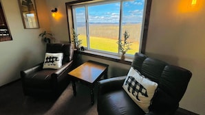 Ein Zimmer mit zwei Ledersesseln, einem kleinen Holztisch und einem großen Fenster mit Blick auf ein Feld.