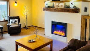 Ein Wohnzimmer mit Kamin, einer Couch, einem Couchtisch, einem an der Wand befestigten Fernseher und einem Holzbalken an der Decke.