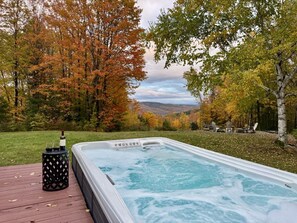 Un jacuzzi en una terraza de madera con vistas a árboles otoñales y un paisaje lejano.