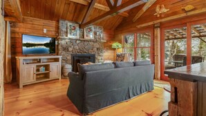 L’intérieur chaleureux d’un chalet avec une cheminée en pierre, une grande fenêtre et un plafond en bois.