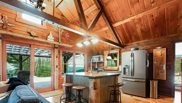 Une cabane en bois comprenant une cuisine, un coin bar et une grande fenêtre donnant sur une forêt.