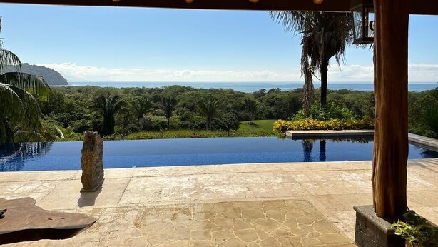 Uma piscina de pedra com vista clara para uma paisagem exuberante e uma cordilheira distante.