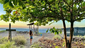 Uma trilha de praia com um poste de madeira, uma estrutura de madeira e vista para o oceano.