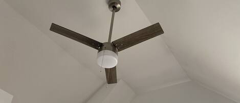 A ceiling fan with three blades and a light fixture in a room with white walls and a window with curtains.