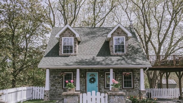 A two-story stone house with a stone facade, a blue door, and a white picket fence.