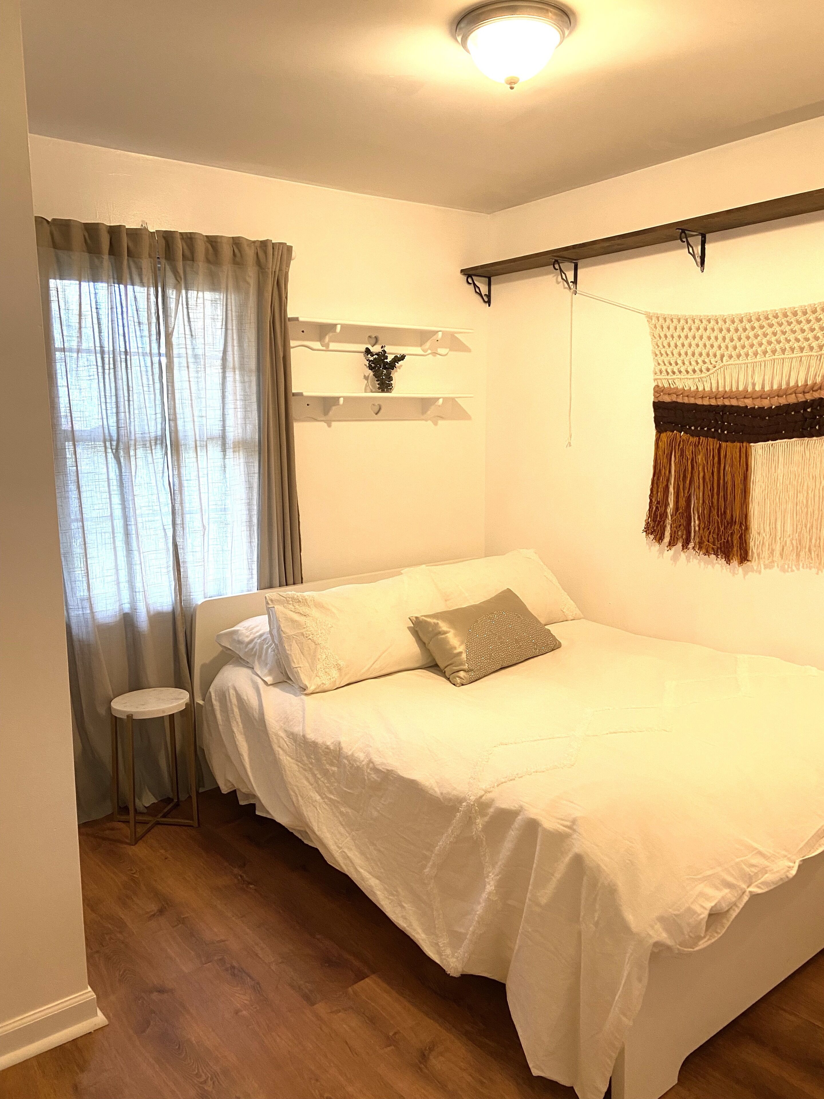 Ein Schlafzimmer mit einem Bett, einem kleinen Hocker, einem Regal mit Dekoration und einer Wanddekoration.