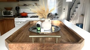 A kitchen with a wooden tray on the counter, a white pitcher, and two bottles of oil.