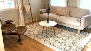 A living room with a beige sofa, a brown leather chair, a round coffee table, a wooden floor, and a patterned rug.