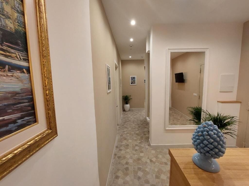 A hallway with a patterned floor, a framed painting on the left, and a decorative sculpture on a table.