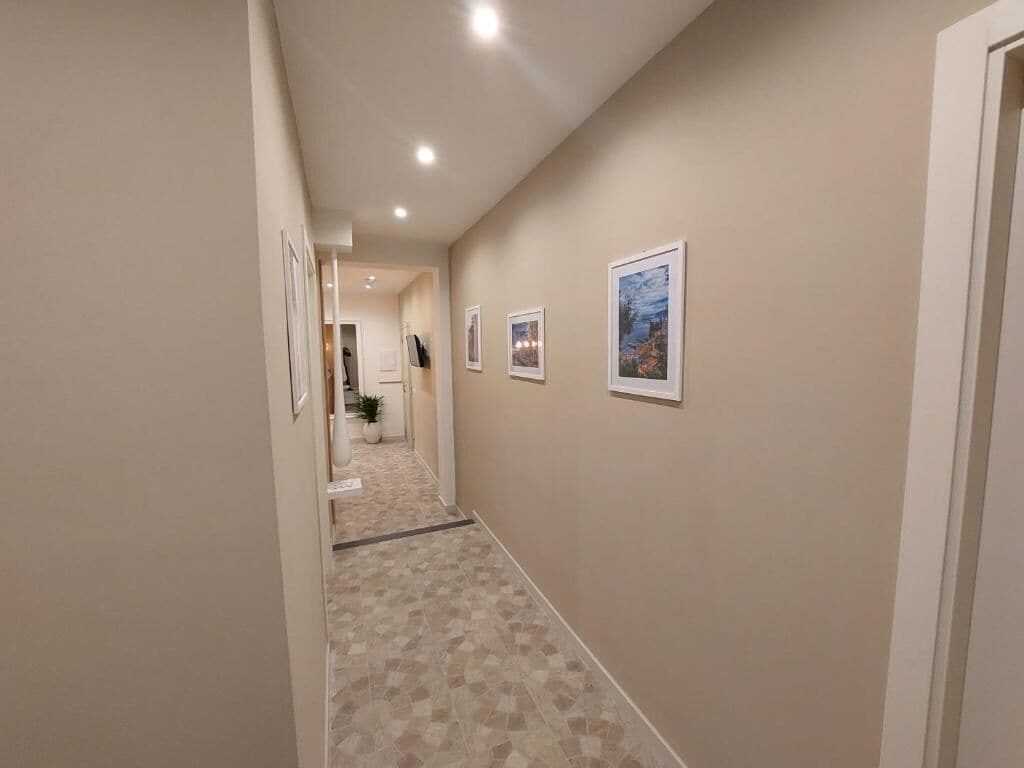 A hallway with beige walls, a tiled floor, and framed pictures on the wall.