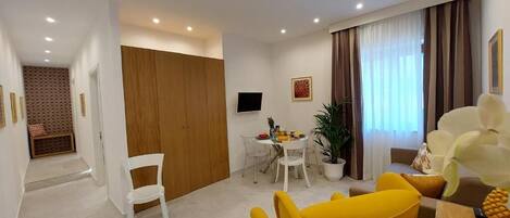 Una sala de estar moderna con comedor, un armario de madera, un televisor y una planta en maceta.