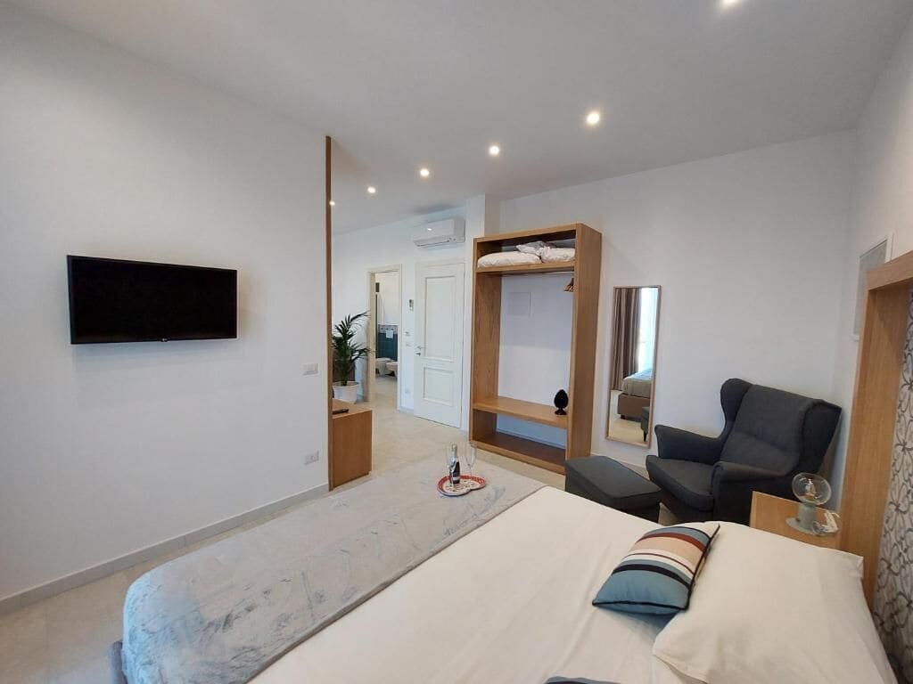 Un dormitorio moderno con cama, televisión, sillón y una pequeña mesa.