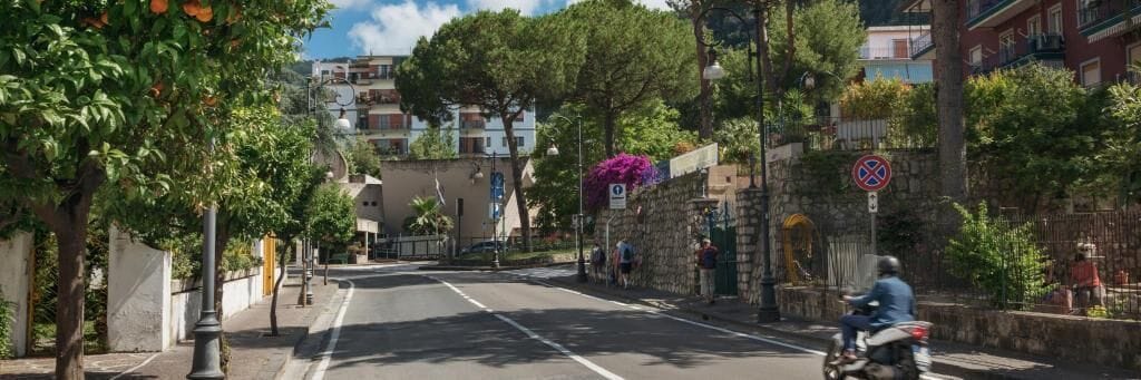 Eine Straße mit Gebäuden, Bäumen und einem Motorradfahrer.