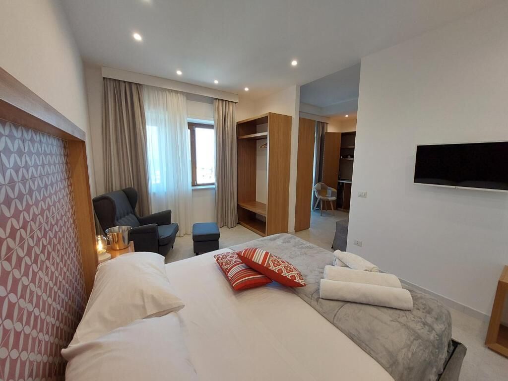 Una habitación de hotel moderna con una cama grande, una zona de estar con una silla, un armario y un televisor montado en la pared.