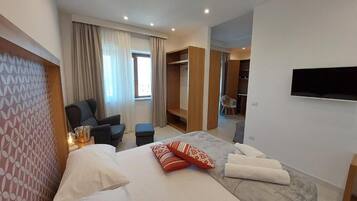 Una habitación de hotel moderna con una cama grande, una zona de estar con una silla, un armario y un televisor montado en la pared.