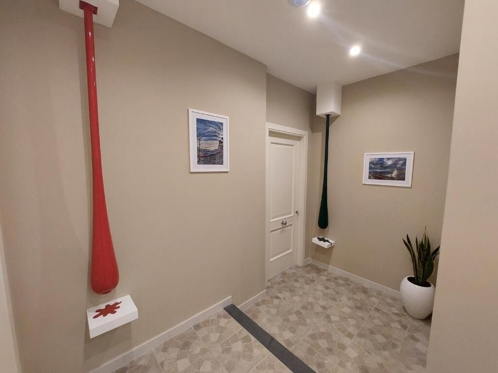 Un couloir aux murs de couleur beige, avec un sol carrelé, une chauve-souris rouge décorative et une plante en pot.