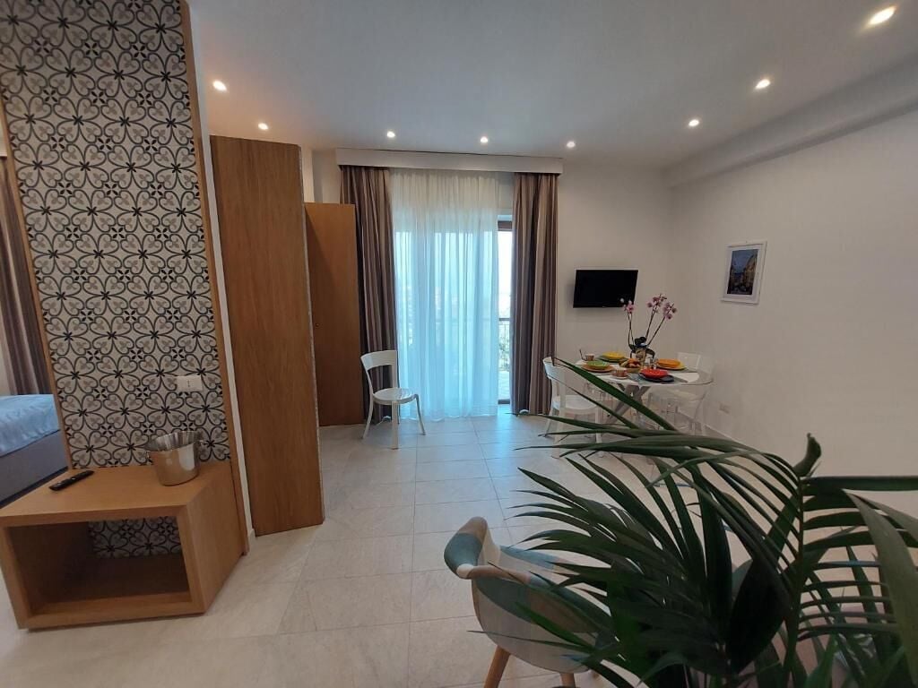 Uma sala de estar moderna com um sofá, uma mesa de jantar com cadeiras, uma televisão e uma planta grande.