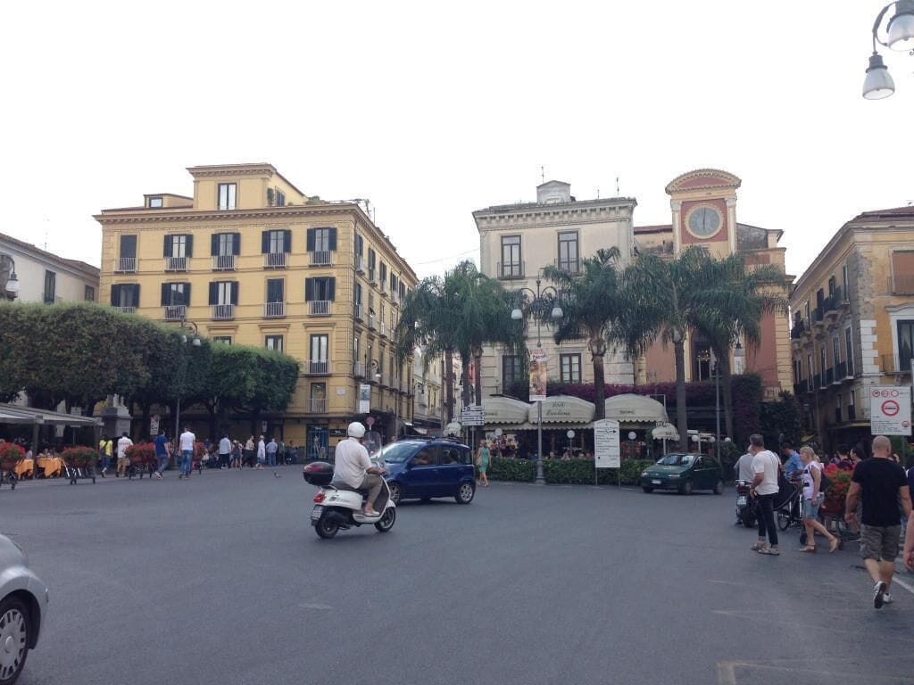 A busy urban street with pedestrians, a scooter, and cars.
