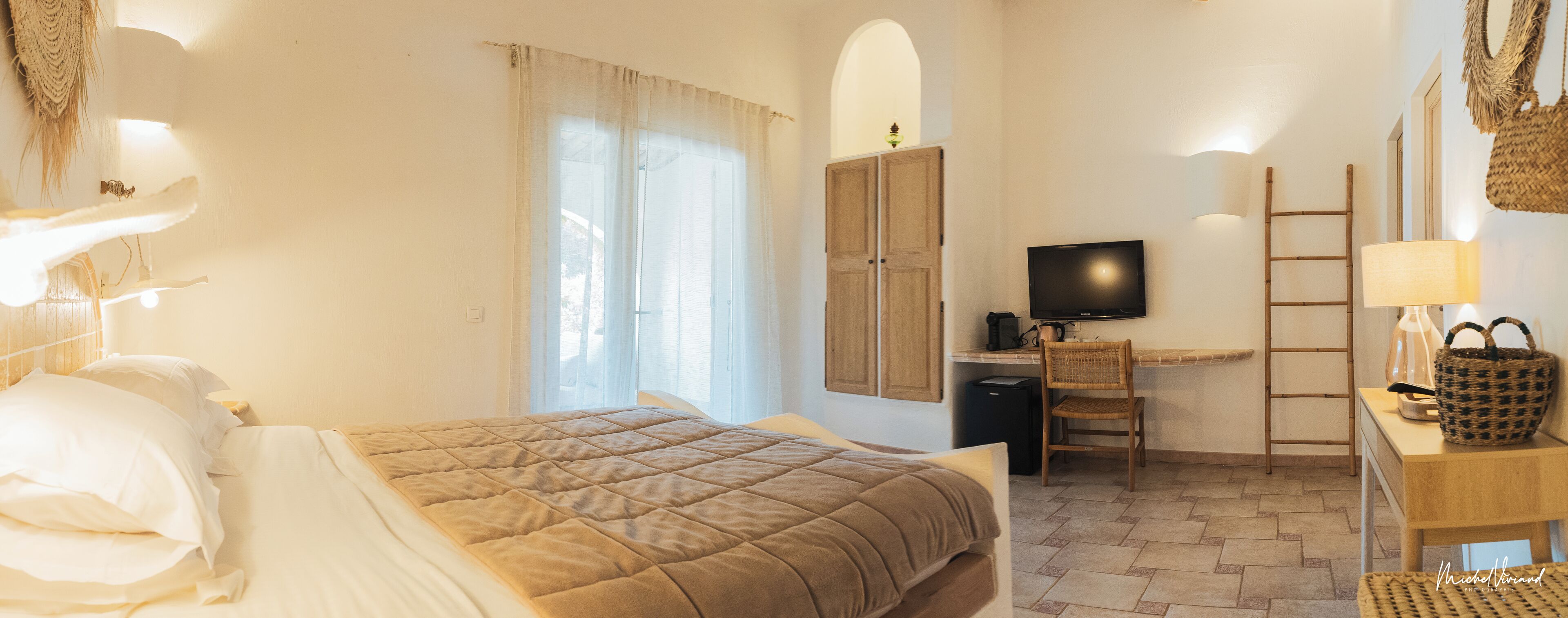A hotel room with a bed, a desk with a computer, a television, and a chair.