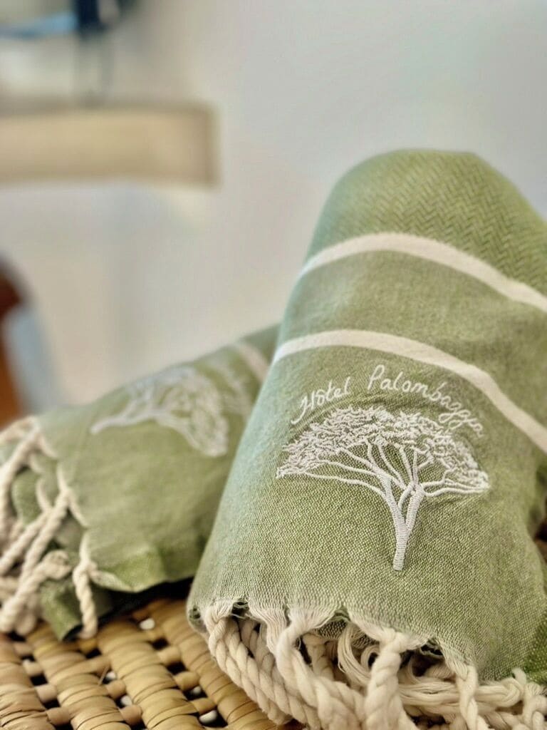 A green towel with a tree embroidery and the text 'Hotel Palombaggia' on it.