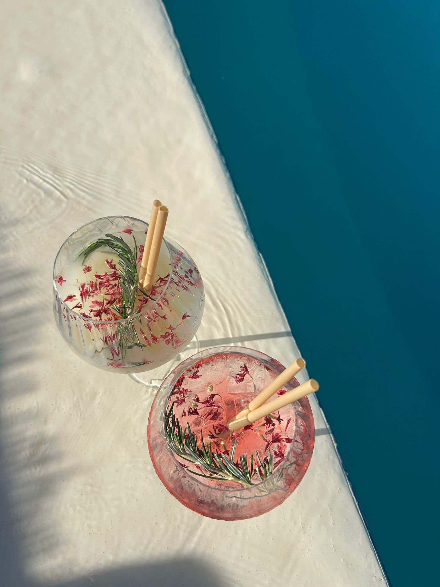Two glass bowls with floral patterns and wooden sticks, placed on a white surface near a pool.