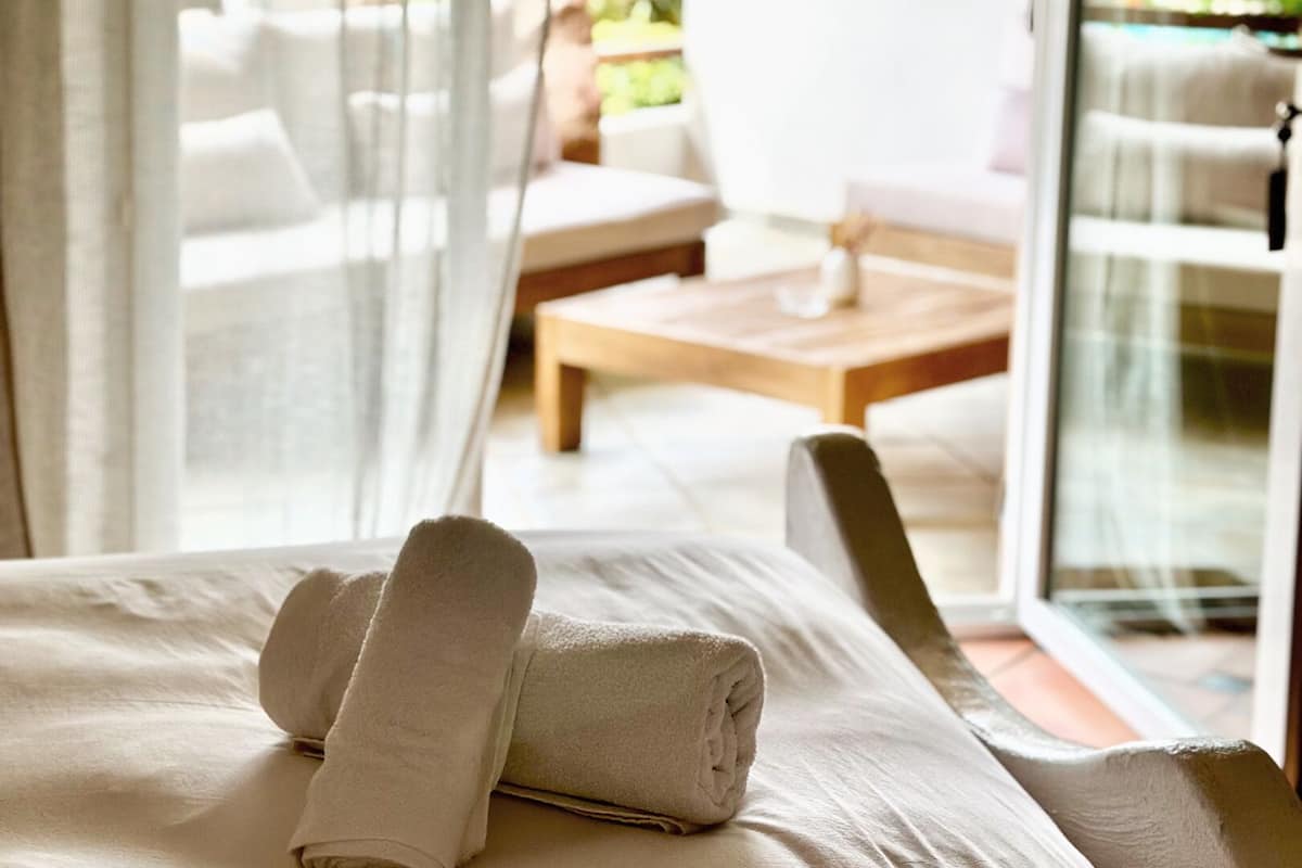 A hotel room with a bed, a wooden table, and a white chair.