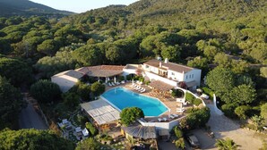An aerial view of a resort with a swimming pool, lounge areas, and a mountainous backdrop. - Hotel Palombaggia (Porto-Vecchio)