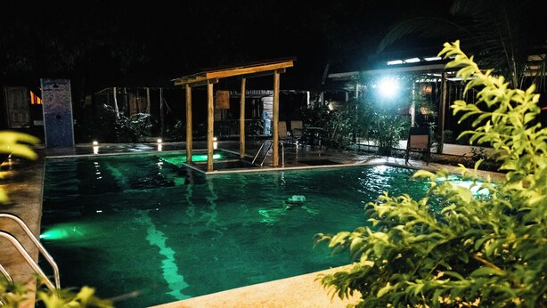 A nighttime pool area with a covered seating area and a pool ladder.