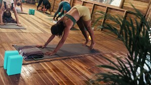A group of people doing yoga in a room with wooden floors and large windows.