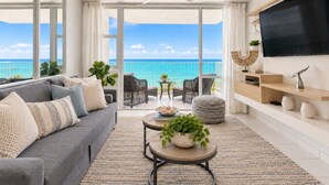 A spacious living room with a large window overlooking the ocean, a ceiling fan, a flat-screen TV, and a comfortable seating area. - Beachfront 2b/2b  Walk 2 Eat  Isla Verde Beach (Carolina)