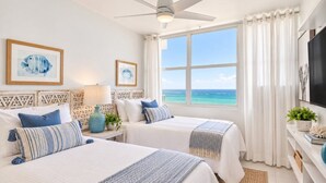 A hotel room with two beds, a ceiling fan, a large window with a view of the sea, and a TV on the wall. - Beachfront 2b/2b  Walk 2 Eat  Isla Verde Beach (Carolina)