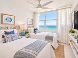 A hotel room with two beds, a ceiling fan, a large window with a view of the sea, and a TV on the wall. - Beachfront 2b/2b  Walk 2 Eat  Isla Verde Beach (Carolina)