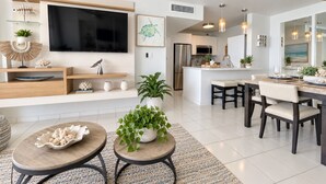 A modern living room with a flat-screen TV, a dining area with a table and chairs, and a kitchen with a refrigerator. - Beachfront 2b/2b  Walk 2 Eat  Isla Verde Beach (Carolina)