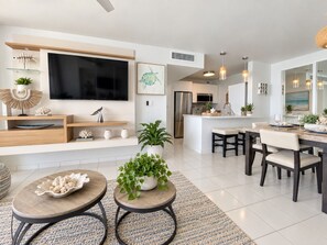 A modern living room with a flat-screen TV, a dining area with a table and chairs, and a kitchen with a refrigerator and stove. - Beachfront 2b/2b  Walk 2 Eat  Isla Verde Beach (Carolina)