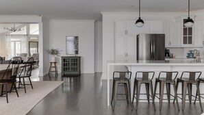 Eine moderne Küche mit weißen Schränken, einem Edelstahlkühlschrank und einer Bar mit Hockern.