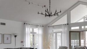 Ein geräumiges Wohnzimmer mit einem grauen Ecksofa, gemusterten Sessel, einem Couchtisch und einer Kronleuchter.