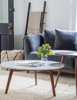 Ein modernes Wohnzimmer mit einem grauen Sofa, einem runden Couchtisch mit einem Buch und einer Vase mit Blumen.