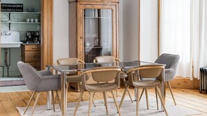 Un espace repas avec une table et des chaises en bois, un lustre, et une vue sur la cuisine et le salon.