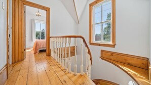 Une pièce avec un escalier en bois, un lit recouvert d’une couverture à pois et une fenêtre donnant sur les arbres.