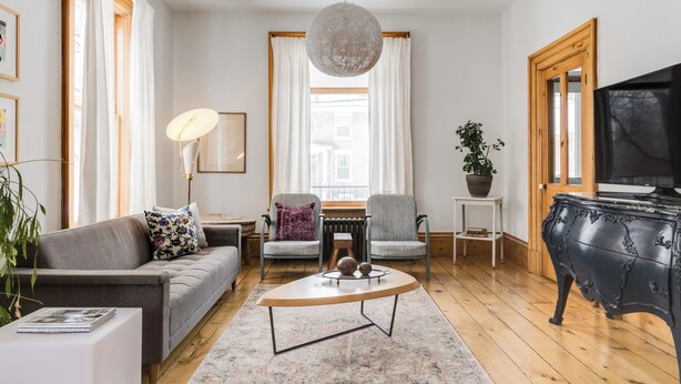 Un salon moderne avec un canapé, des fauteuils, une table basse, un téléviseur et une plante en pot.