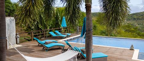 A wooden deck with lounge chairs and a hammock, overlooking a swimming pool.