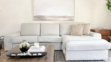 Un salon avec un canapé gris, une table basse agrémentée d’objets décoratifs, une table d’appoint et une œuvre d’art encadrée accrochée au mur.