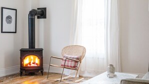 Una sala de estar acogedora con una estufa de leña, un sillón mecedor y una mesa con un jarrón.
