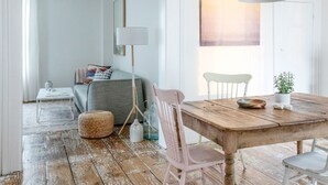 Una habitación acogedora con una mesa de comedor de madera, una lámpara blanca, un sofá gris y una planta pequeña sobre la mesa.