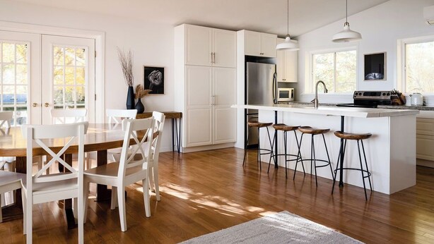 A modern kitchen with white cabinetry, a central island with bar stools, a stainless steel refrigerator, and a microwave. - The Wilolea | Milford | 5 Bedrooms | Waterfront (Prince Edward)