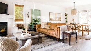 A living room with a leather sofa, a coffee table, a fireplace, a dining area with a table and chairs, and a TV mounted on the wall. - The Addison | Modern Farmhouse | Pool  and  Hot Tub (Prince Edward)