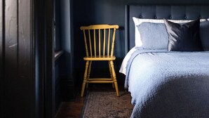 Une chambre avec une chaise en bois, un lit recouvert d’une couverture bleue et un tapis à motifs.