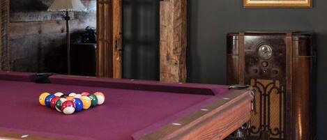 A pool table with balls, a vintage radio, and a framed picture on the wall.