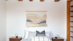 A bedroom with a bed, two nightstands, a wall tapestry, and a wooden ceiling beam.